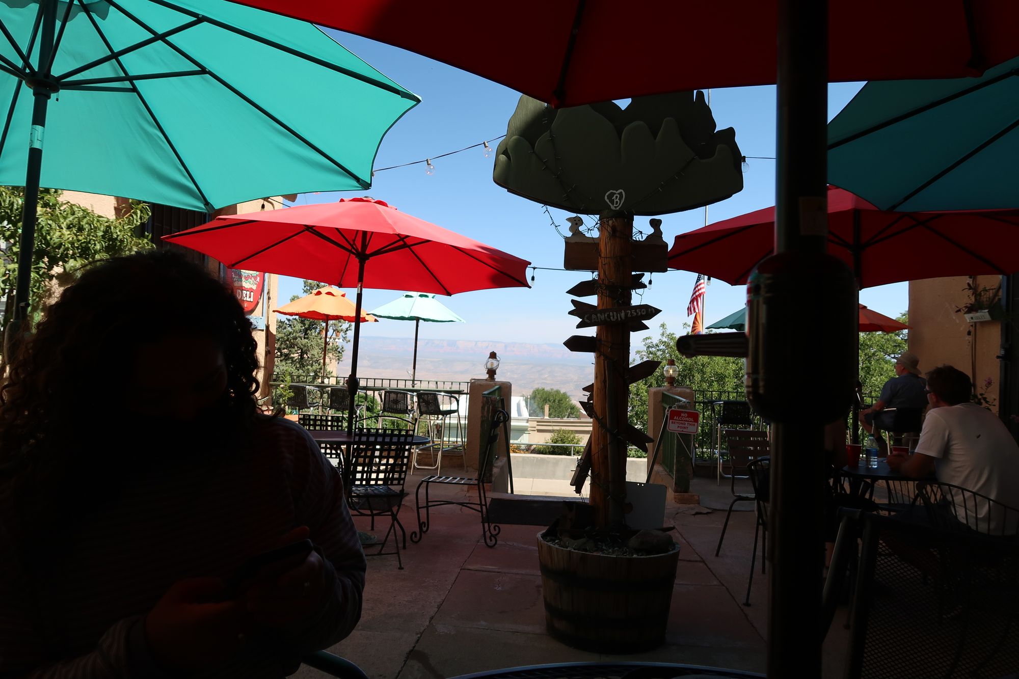 girl sitting in shadows of Hilltop Deli in Jerome Arizona with brighty colored umbrellas