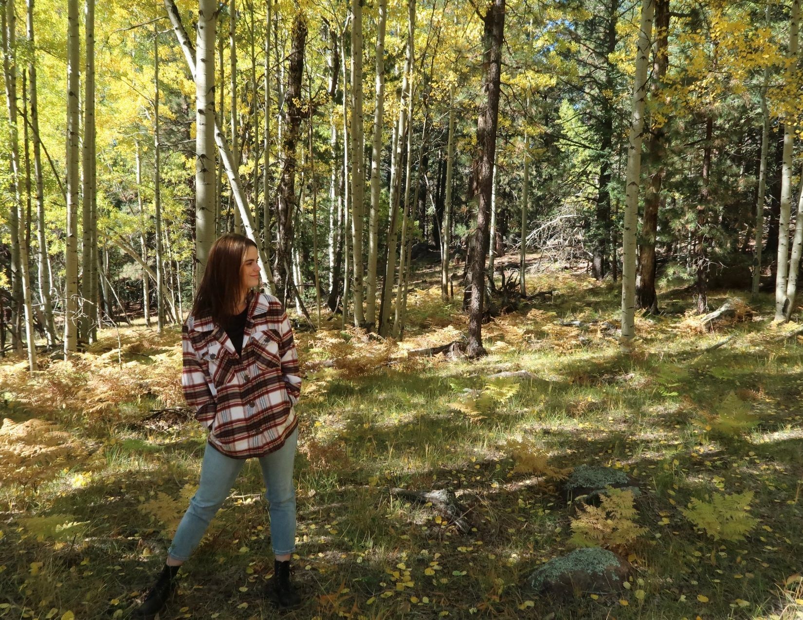 A young woman dressed in warm clothes standing in the Aspens in Flagstaff Arizona 