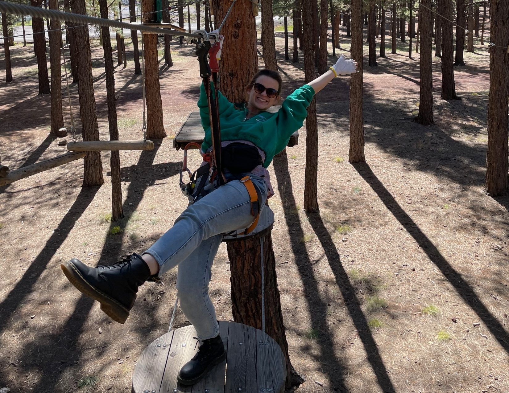 A young woman hanging from an obstacle course attached to Ponderosa Pine trees in Flagstaff, Arizona.