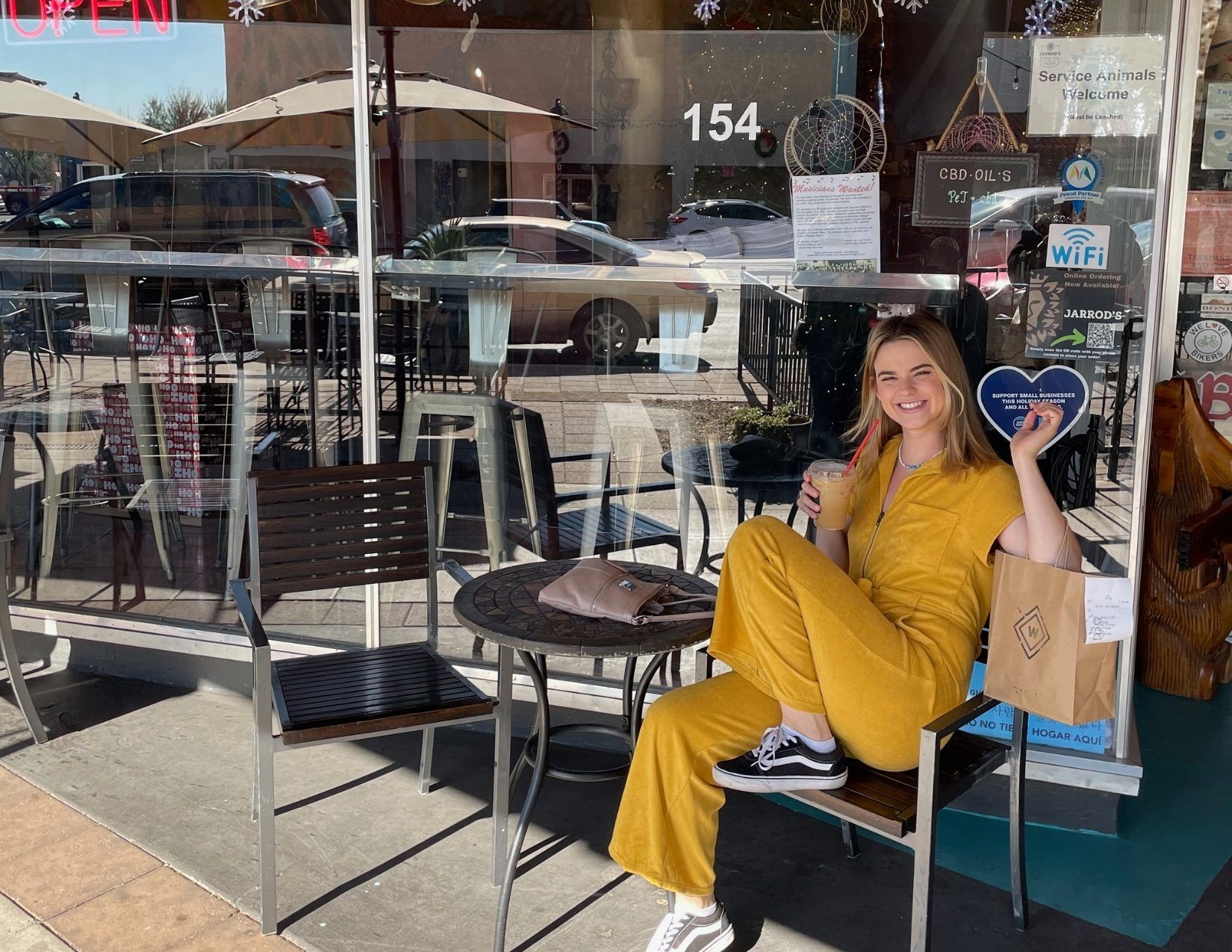 a girl sitting outside of a coffee shop enjoyed an iced coffee wearing all yellow