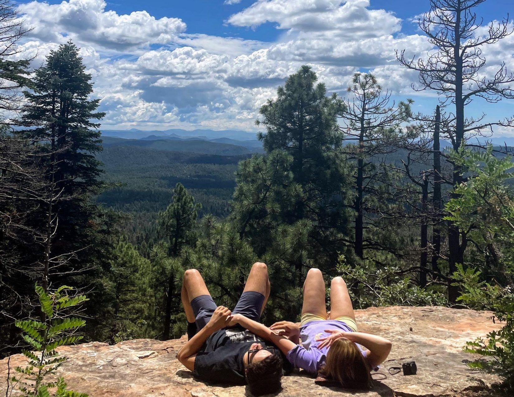 a young man and young girl laying on a rock, looking at the blue sky, surrounded by tress in Payson Arizona