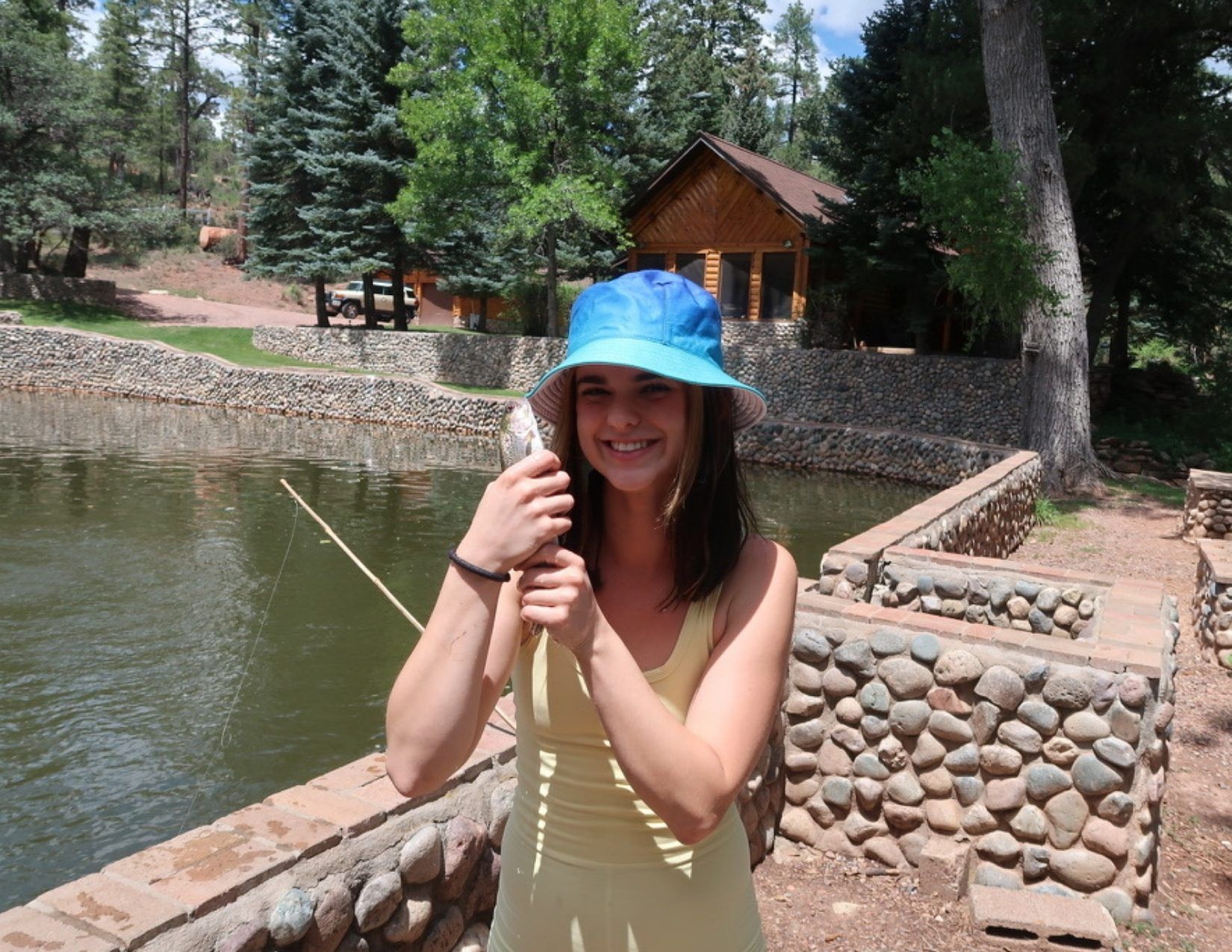Young girl smiling hoding a trout in front of a pond and fishing pole in Payson Arizona