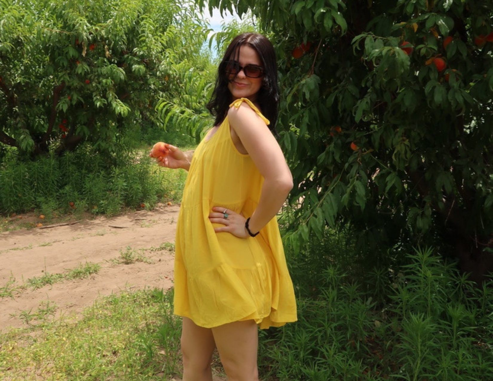 Young Girl in yellow Dress standing with a peach at Schnepf Farm in Mesa Arizona