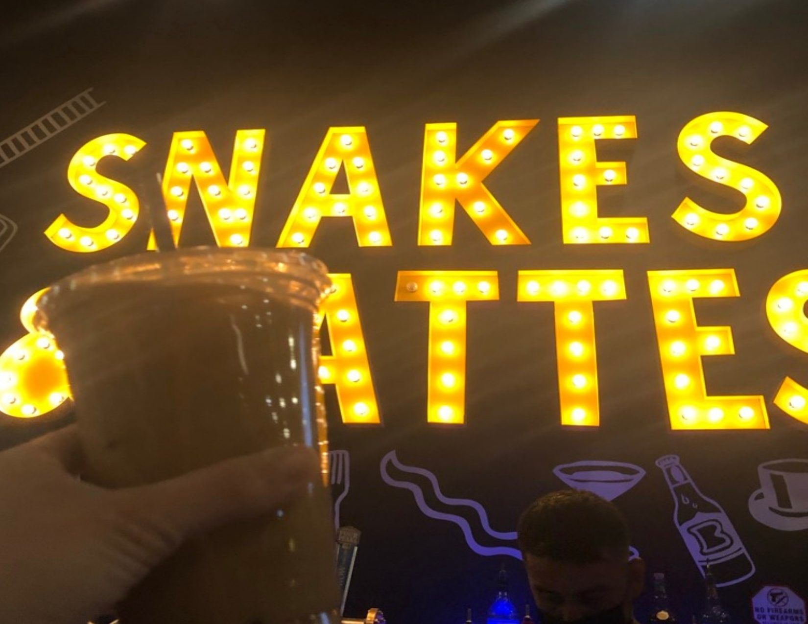 Hand holding a cup of iced coffee in front of the Snakes and Lattes sign in Tempe Arizona