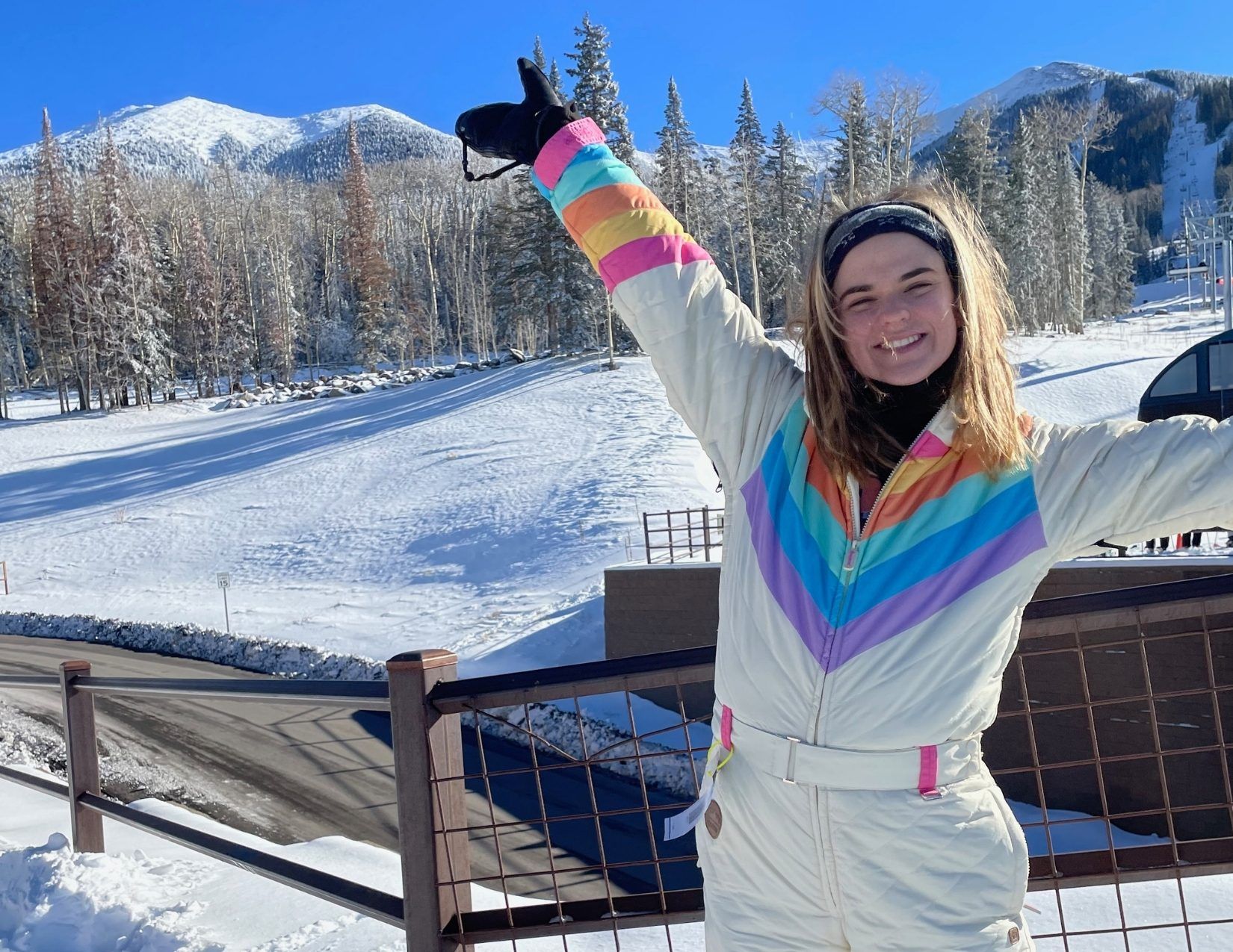 a young woman in a colorful snowsuit smiling in front of snowy mountains at a ski resort in Flagstaff, Arizona