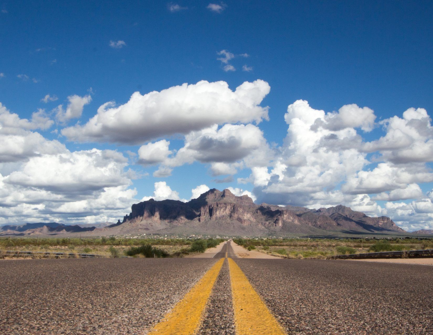 Desert road with superstition mountains in the background and white clouds in the blue sky
