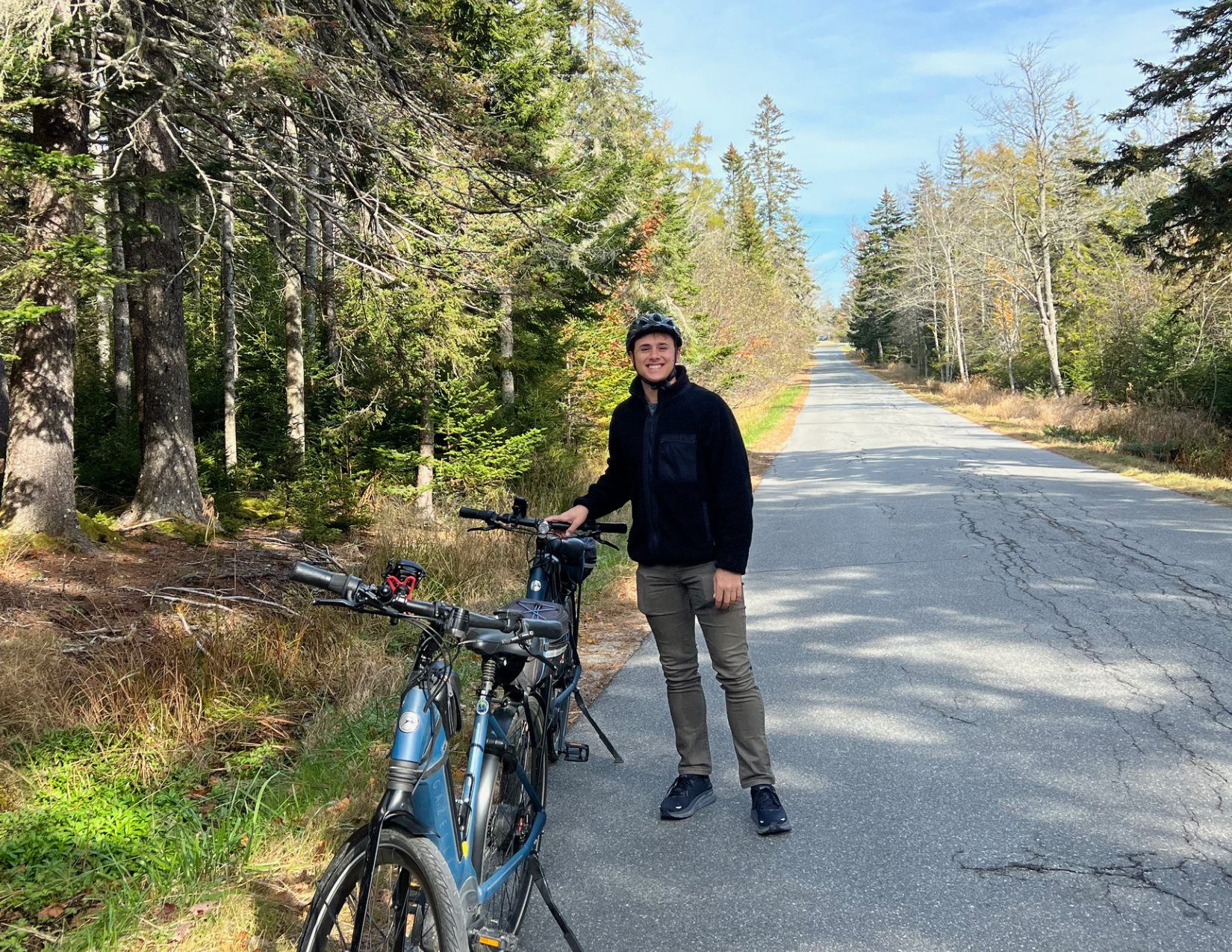 Man smiling next to his ebike on the side of the road, cycling to Acadia National Park, Maine