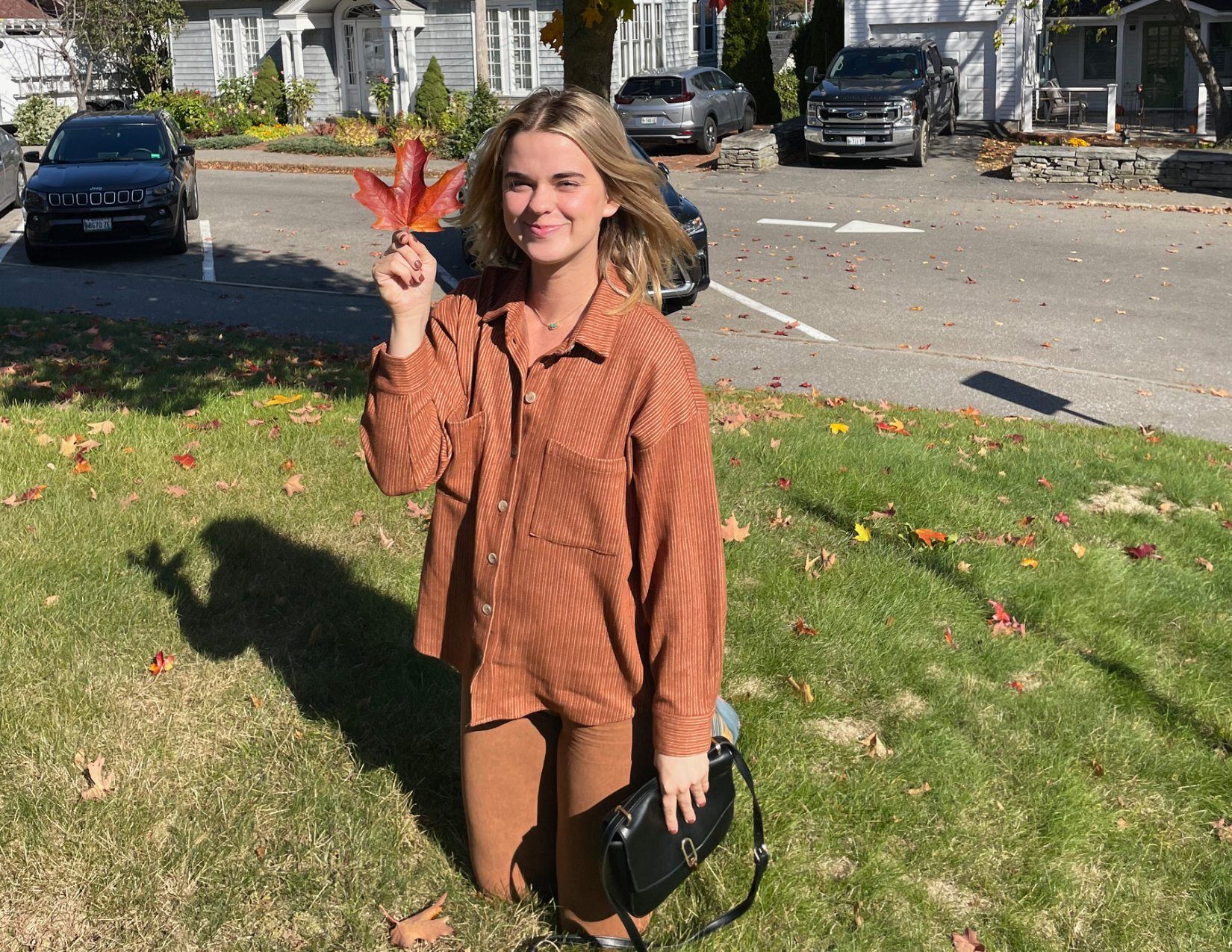 Girl smiling while holding a fallen red maple leaf during the fall in Camden, Maine