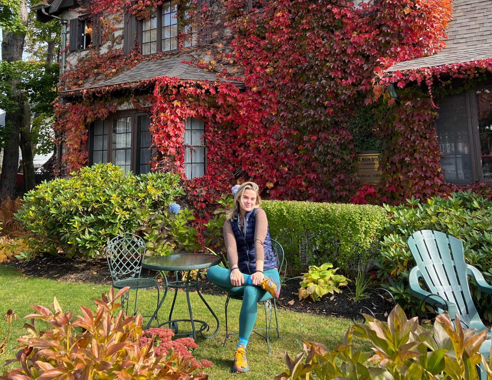 A woman sitting at a coffee table outside of an old inn covered in red ivy leaves in Bar Harbor, Maine