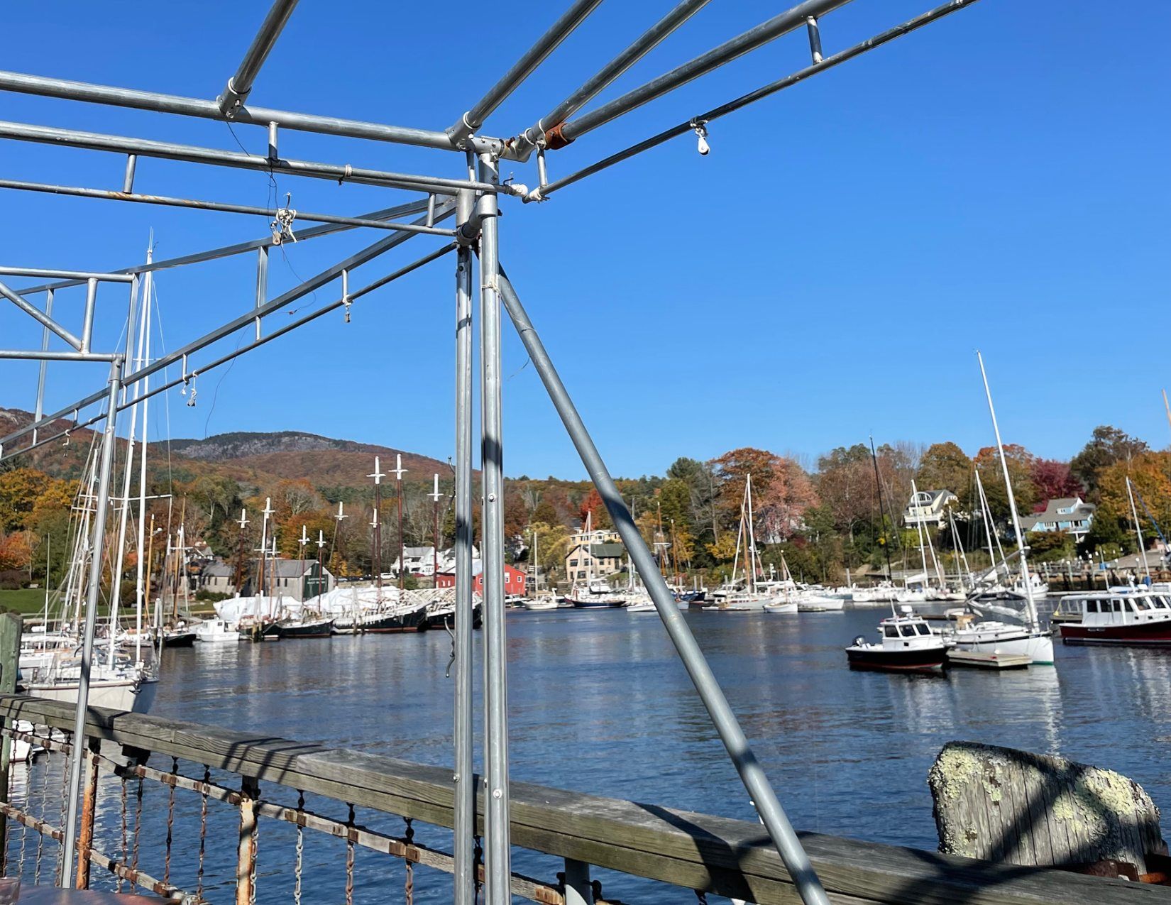 View of boats docked in a marina in Camden, Maine with fall trees surrounding the water