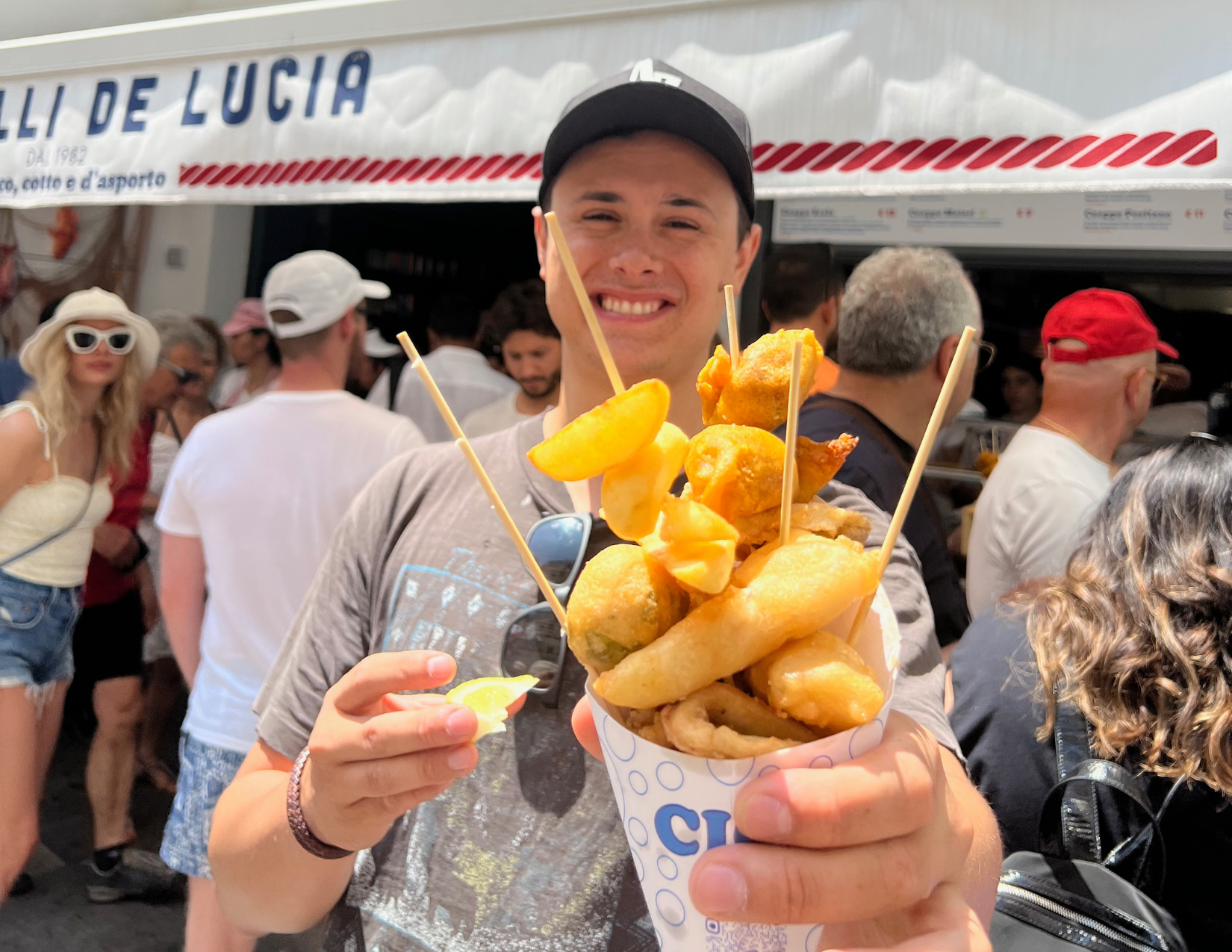 A man smiling while holding out his cone of fried seafood from a street restaurant in Amalfi, Italy