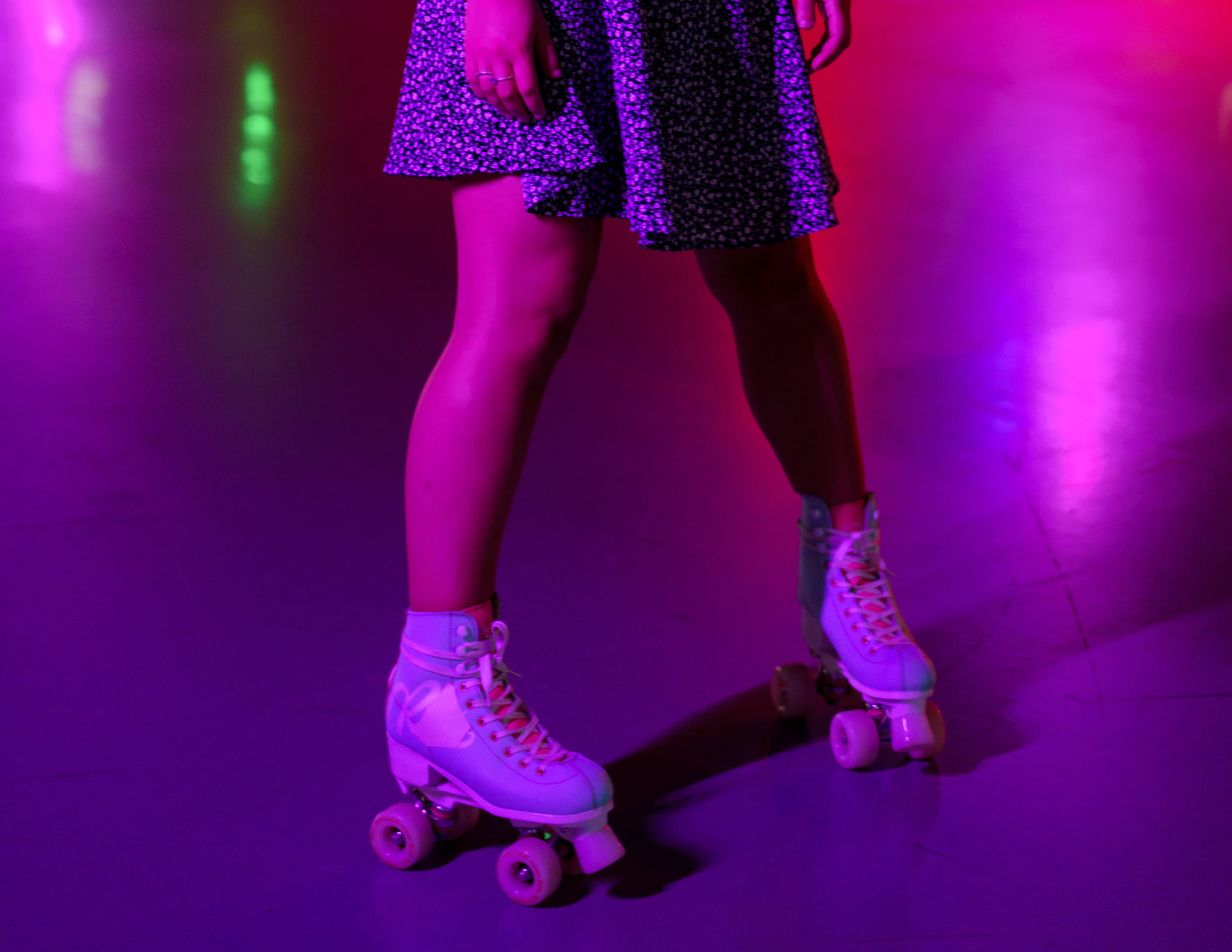 Photo of the bottom half of a women in a dress roller skating in neon lights