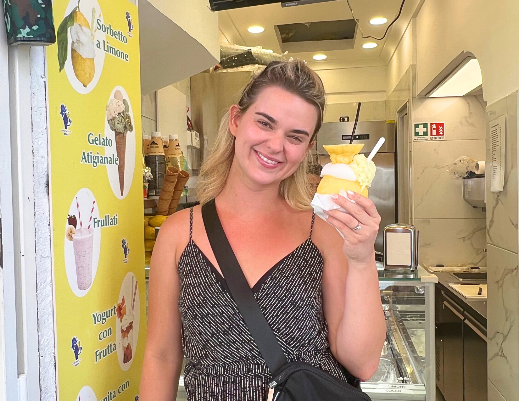 A woman smiling with holding lemon sorbet stuffed inside of a lemon at a gelateria in Amalfi, Italy