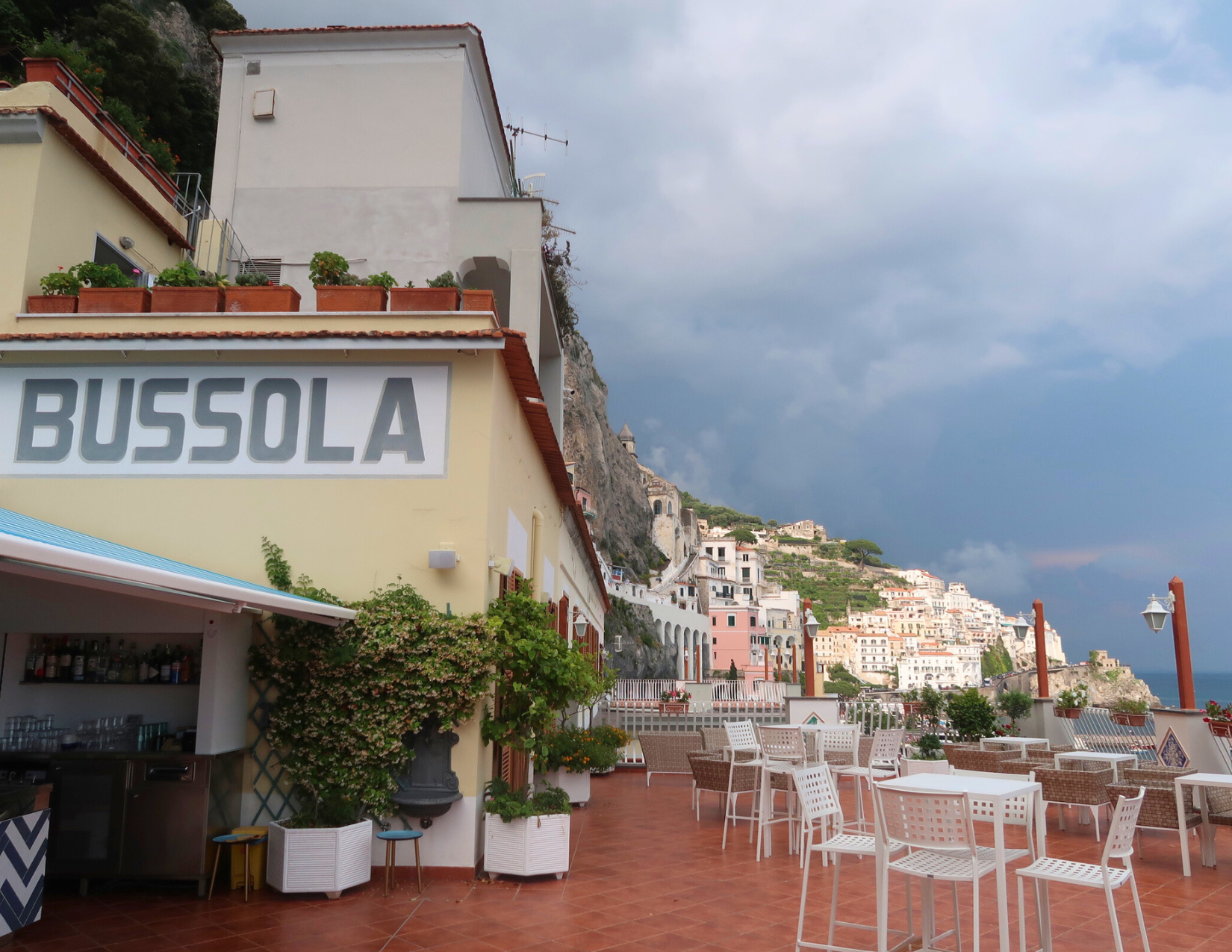 A rooftop bar on top of a hotel, with views of the Tyrrhenian Sea and the white and tan buildings lining the coast.