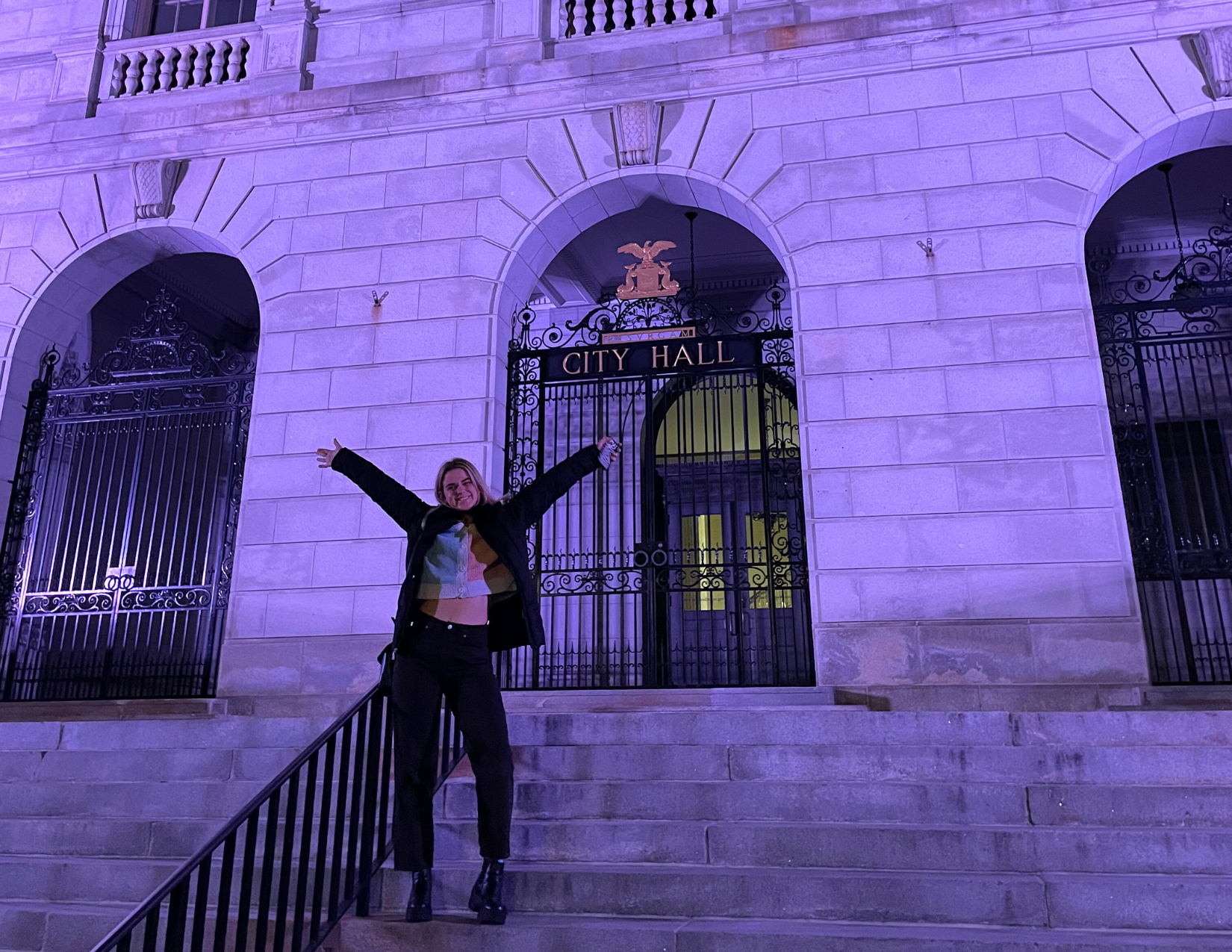 A woman smiling with her hands up in excitement during her first trip to Portland, Maine in front of City Hall