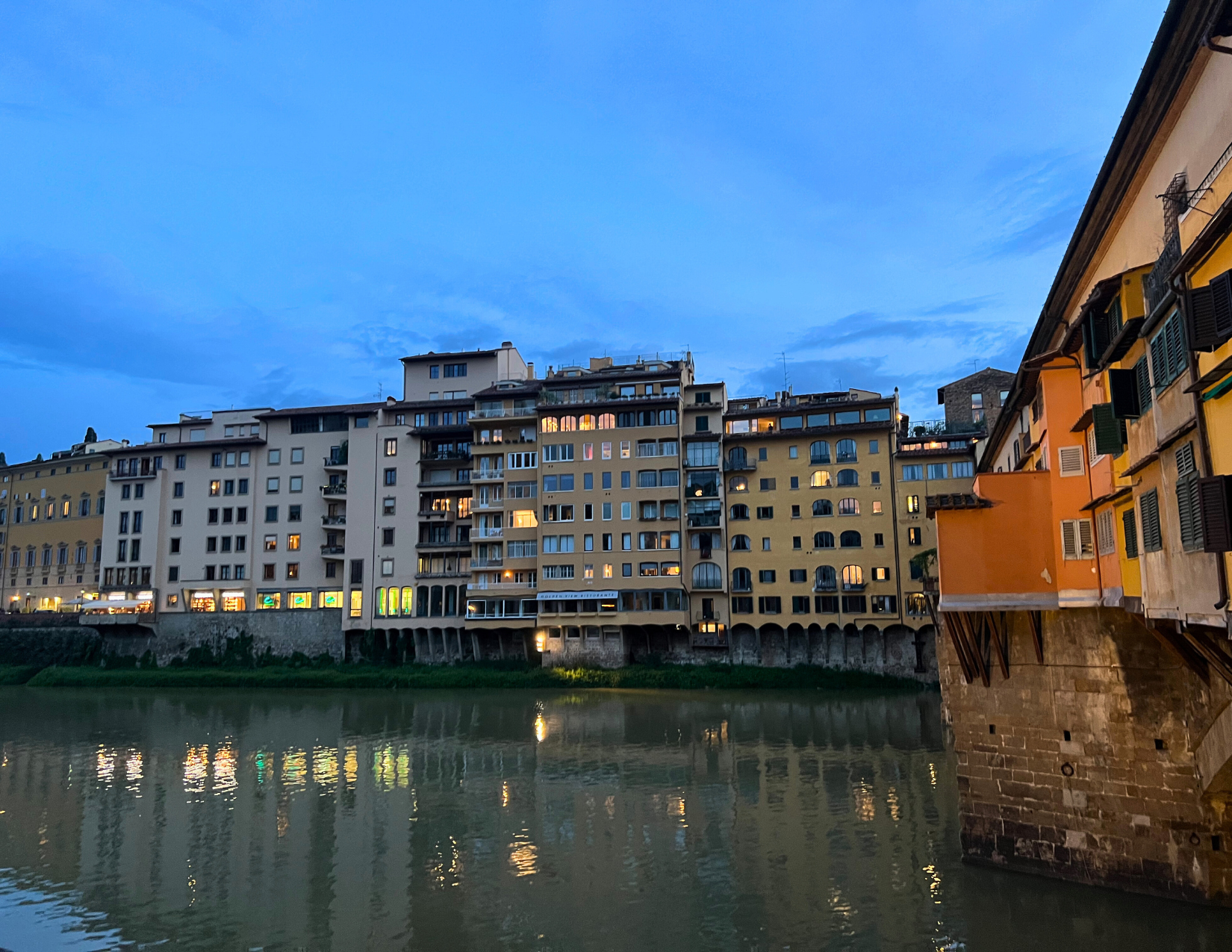 Grouping of tan and white buildings overlooking the Arno River at dusk in Florence, Italy