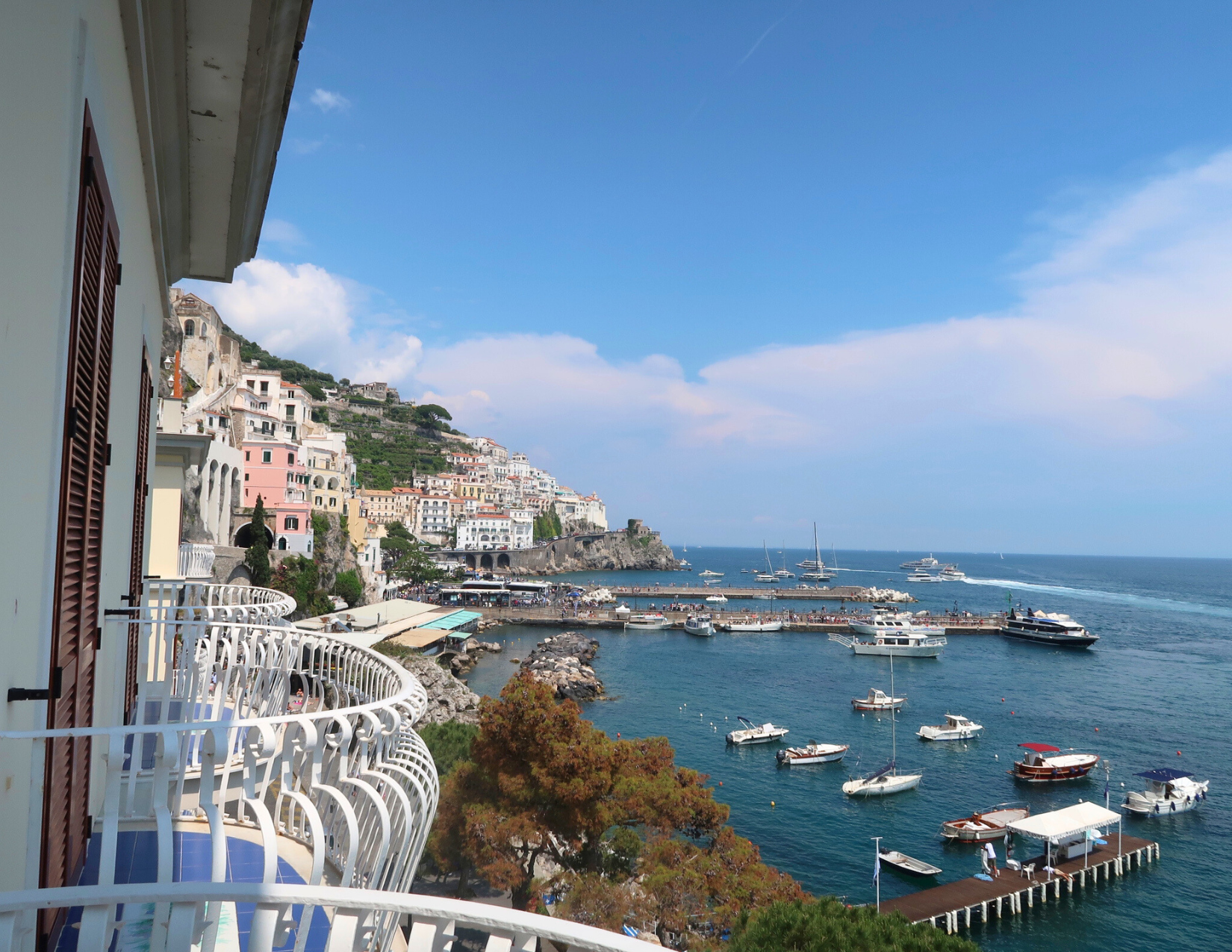 White half circle railings on the balconies of a hotel in Amalfi, Italy, with a view of the Tyrrhenian Sea and the colorful buildings lining the coast.