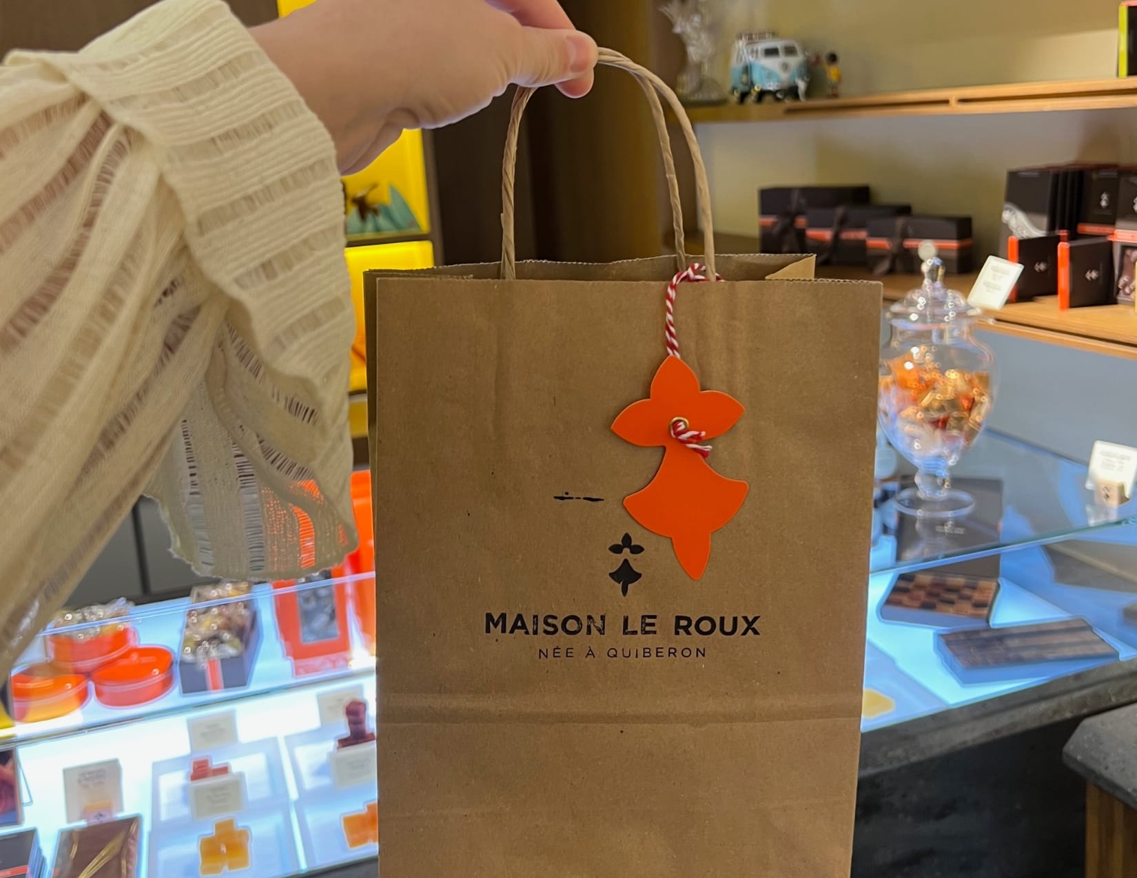 woman holding up paper bag of caramels and sweets from Maison le Roux in Paris, France