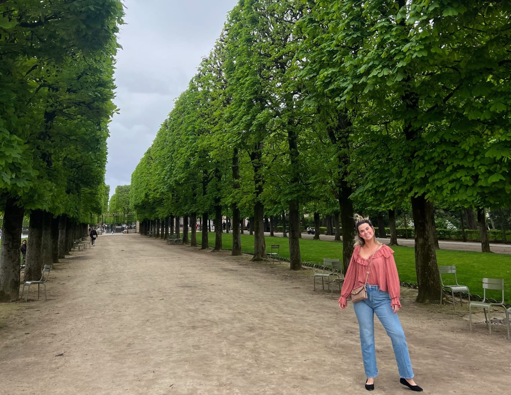 Woman in pink shirt standing next to manicured trees at the Jardin du Luxembourg in Paris, France