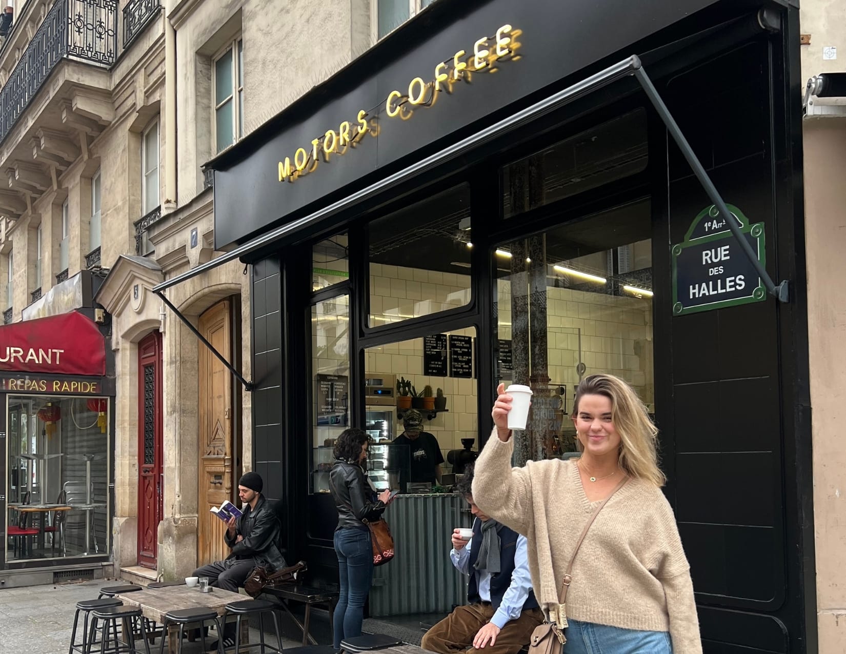 Woman holding small cup standing outside of Motors Coffee in Paris, France