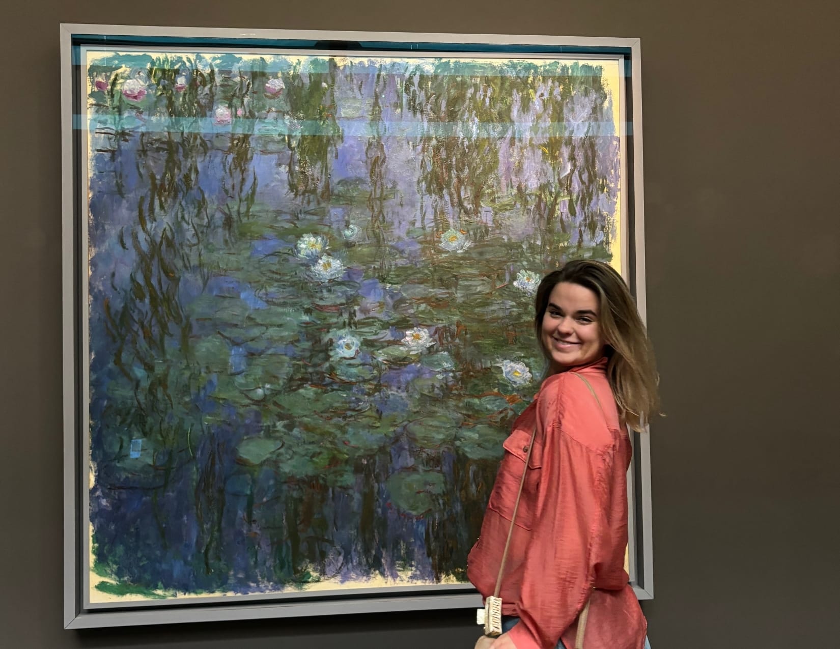 Woman in orange shirt standing in from of Nymphéas bleus painting by Claude Monet at the Musee d'Orsay in Paris, France