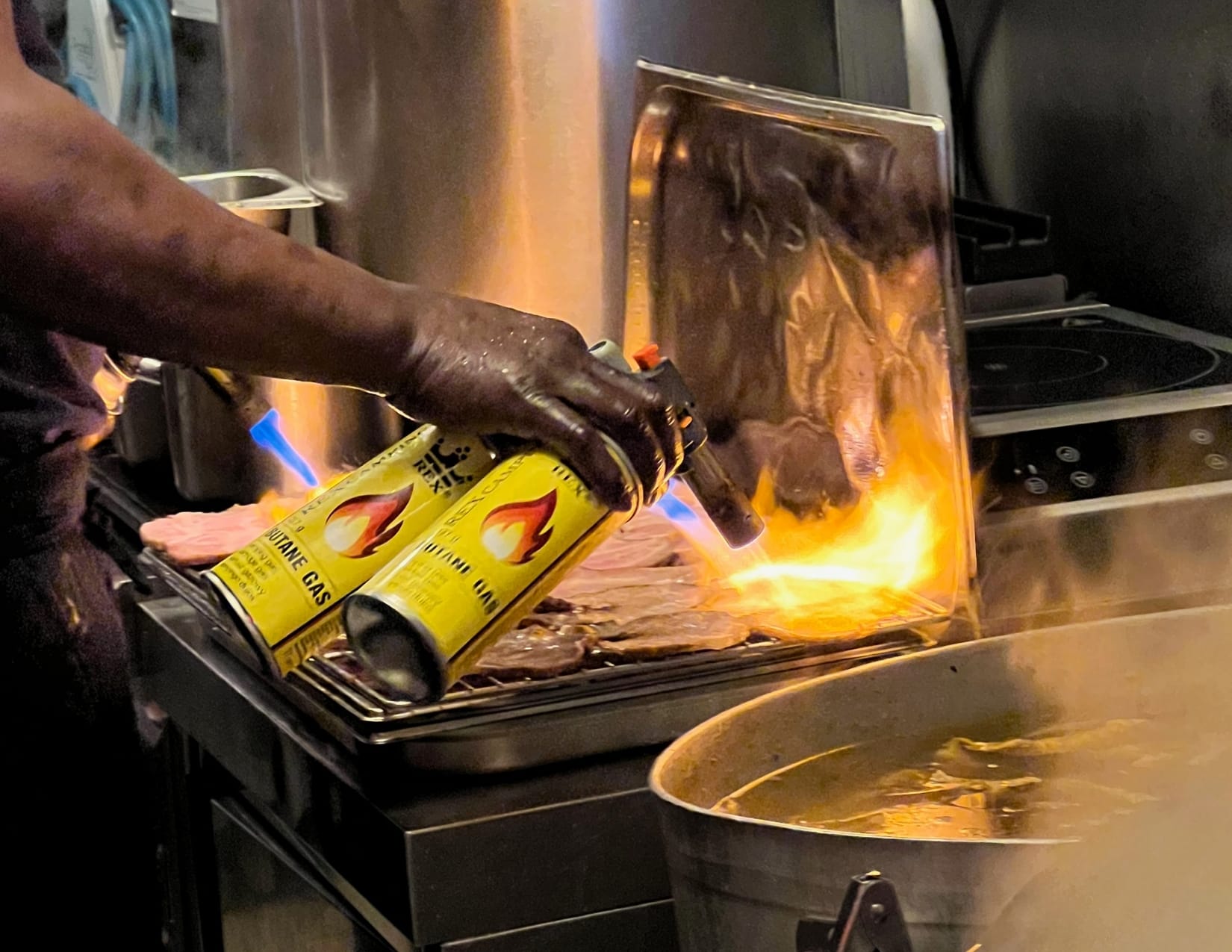 Cook using butane gas to cook pork cutlets at Kodawari Ramen in Paris, France