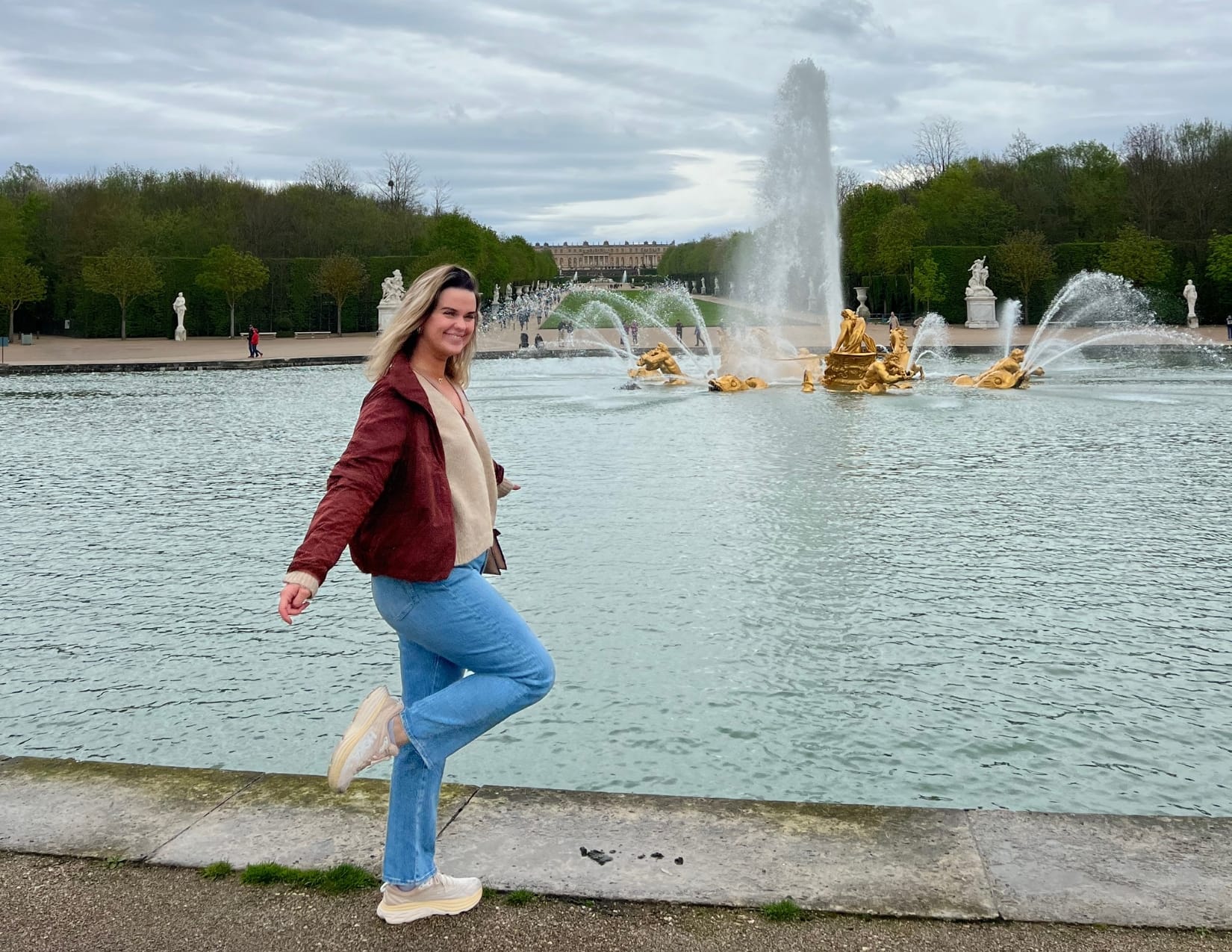 Woman in red jacket standing in front of the Apollo Fountain at the Gardens of Versailles in Paris, France 