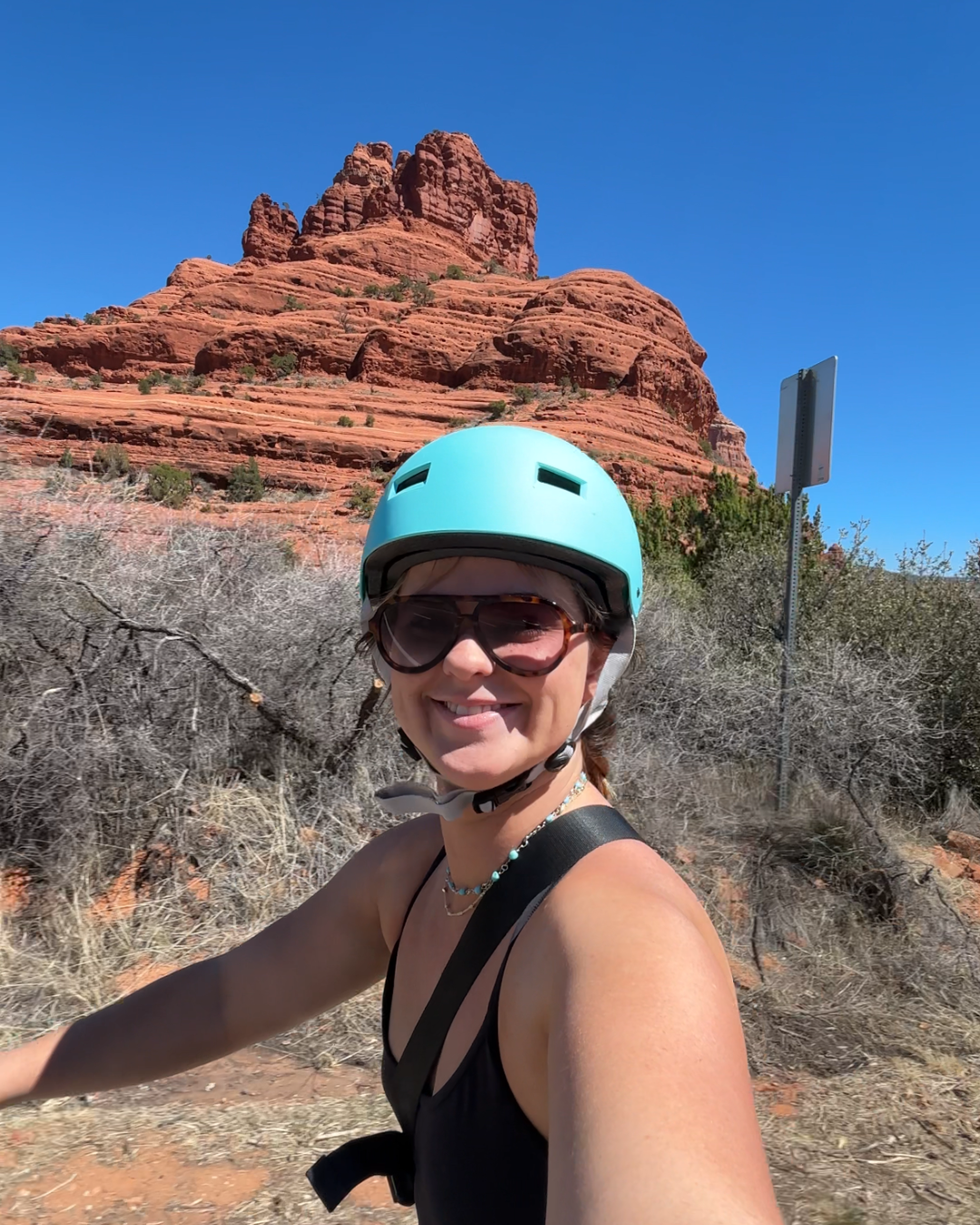 Woman on bike with turquoise helmet smiling in front of Bell Rock in Sedona, Arizona