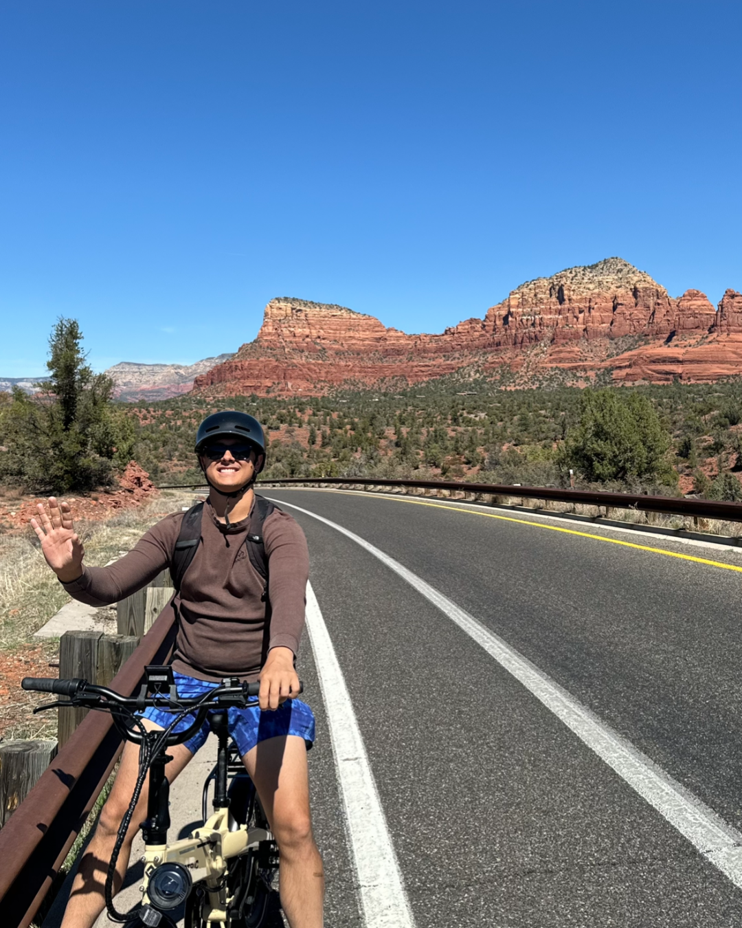 man in brown shirt and blue shorts on the road with red rocks in background