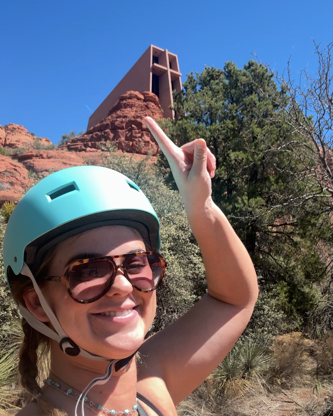 girl with helmet smiling pointing to a chapel in the mountains