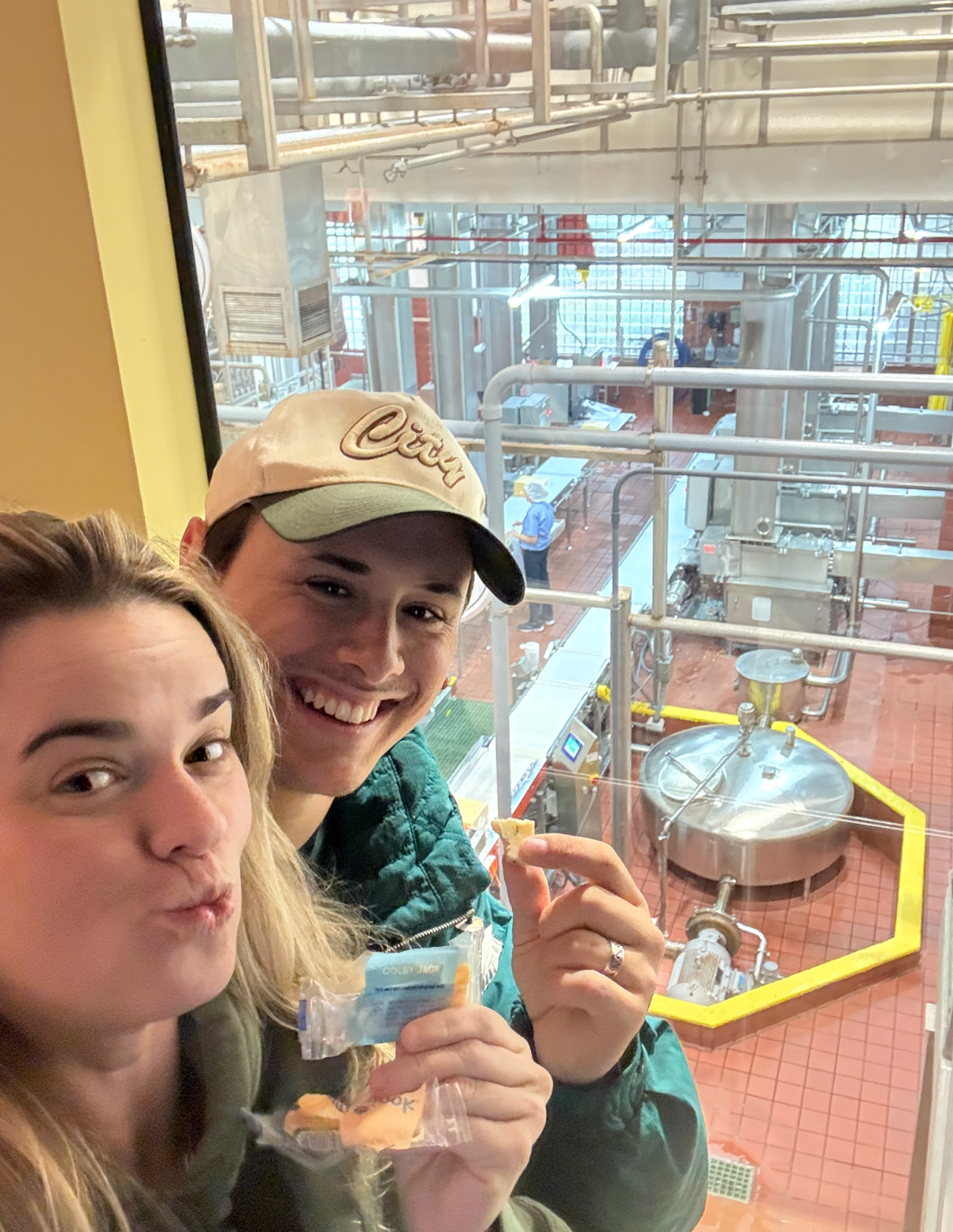 A Man and a Woman posing with pieces of cheese in front of the factory floor at Tillamook Creamery in Tillamook, Oregon